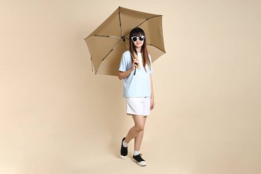 Mavi polo tişörtlü, beyaz şortlu, bej arka planda Şemsiye tutan Asyalı bir kadın. Üniversite öğrencisi, Gen Z