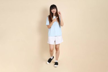 Açık mavi polo tişörtlü, beyaz şortlu, elinde düz bej bir kalem tutan genç Asyalı bir kadın. Üniversite öğrencisi, Gen Z, Summer