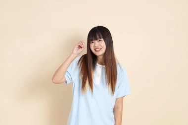 Açık mavi polo tişörtlü, beyaz şortlu, elinde düz bej bir kalem tutan genç Asyalı bir kadın. Üniversite öğrencisi, Gen Z, Summer