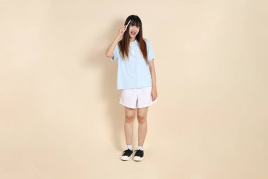 Açık mavi polo tişörtlü, beyaz şortlu, elinde düz bej bir kalem tutan genç Asyalı bir kadın. Üniversite öğrencisi, Gen Z, Summer