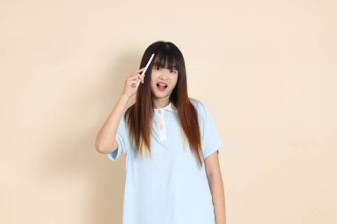 Açık mavi polo tişörtlü, beyaz şortlu, elinde düz bej bir kalem tutan genç Asyalı bir kadın. Üniversite öğrencisi, Gen Z, Summer