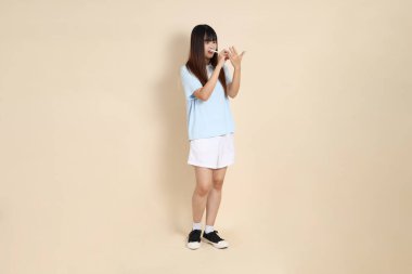 Açık mavi polo tişörtlü, beyaz şortlu, elinde düz bej bir kalem tutan genç Asyalı bir kadın. Üniversite öğrencisi, Gen Z, Summer