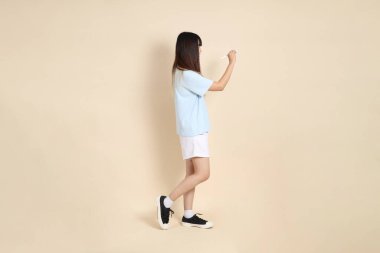 Açık mavi polo tişörtlü, beyaz şortlu, elinde düz bej bir kalem tutan genç Asyalı bir kadın. Üniversite öğrencisi, Gen Z, Summer