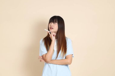 Açık mavi polo tişörtlü, beyaz şortlu, elinde düz bej bir kalem tutan genç Asyalı bir kadın. Üniversite öğrencisi, Gen Z, Summer