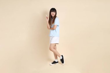 Açık mavi polo tişörtlü, beyaz şortlu, elinde düz bej bir kalem tutan genç Asyalı bir kadın. Üniversite öğrencisi, Gen Z, Summer