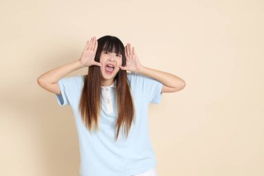 Orta boy Asyalı bir kadının açık mavi polo tişörtü ve beyaz şort giydiği fotoğraf. Sade bir bej arka plan karşısında aptalca ve komik. Üniversite öğrencisi, Gen Z