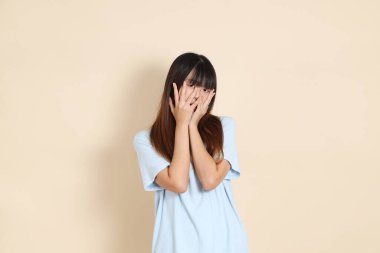 Açık mavi polo tişörtlü, beyaz şortlu, bej arka plandan korkan genç bir Asyalı kadın. Üniversite öğrencisi, Gen Z, Summer