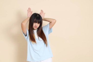 Orta boy Asyalı bir kadının açık mavi polo tişörtü ve beyaz şort giydiği fotoğraf. Sade bir bej arka plan karşısında aptalca ve komik. Üniversite öğrencisi, Gen Z