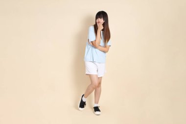 Açık mavi polo tişörtlü, beyaz şortlu, bej renkli arka planı olan genç bir Asyalı kadın. Üniversite öğrencisi, Gen Z, Summer