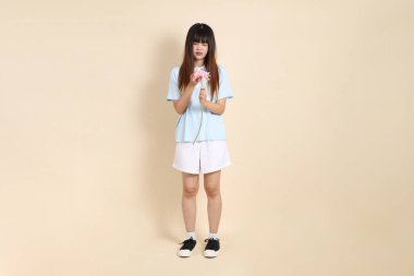 Açık mavi polo tişörtlü, beyaz şortlu, bej arka planda çiçek tutan orta boy bir Asyalı kadın resmi. Üniversite öğrencisi, Gen Z