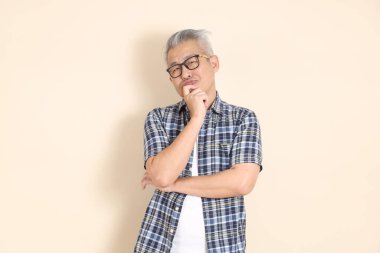 Gözlüklü Asyalı bir son sınıf öğrencisinin portresi. Düşünüyor, ekose gömlek, şort ve spor ayakkabı giyiyor, bej arka planda izole edilmiş. Yaşlı erkek yaşam tarzı konsepti.