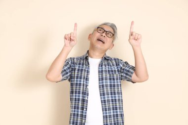 Gözlüklü bir Asyalı 'nın portresi, bej arka planda izole edilmiş, günlük ekose gömlek, şort ve spor ayakkabı giyiyor. Yaşlı erkek yaşam tarzı konsepti.