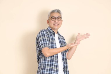 Gözlüklü bir Asyalı 'nın portresi, bej arka planda izole edilmiş, günlük ekose gömlek, şort ve spor ayakkabı giyiyor. Yaşlı erkek yaşam tarzı konsepti.