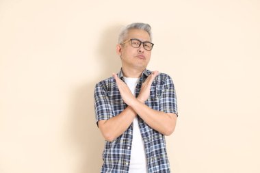 Gözlüklü bir Asyalı 'nın portresi, reddediyor, hayır, günlük ekose gömlek, şort ve spor ayakkabı giyiyor, bej arka planda izole edilmiş. Yaşlı erkek yaşam tarzı konsepti.