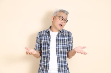 Gözlüklü, Asyalı, yaşlı bir adamın portresi, pardon, önemli değil, günlük ekose gömlek, şort ve spor ayakkabı giyiyor, bej arka planda soyutlanmış. Yaşlı erkek yaşam tarzı konsepti.