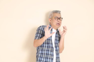 Gözlüklü, korkusuz, sıradan ekose gömlekli, şortlu ve bej arka planda izole edilmiş spor ayakkabılı bir Asyalı 'nın portresi. Yaşlı erkek yaşam tarzı konsepti.