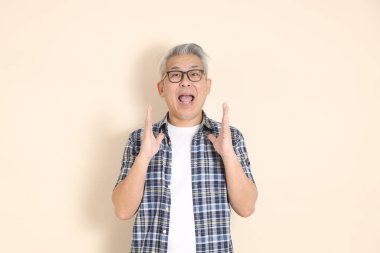 Gözlüklü bir Asyalı 'nın portresi, sürpriz, vay canına, günlük ekose gömlek, şort ve spor ayakkabı giyiyor, bej arka planda izole edilmiş. Yaşlı erkek yaşam tarzı konsepti.