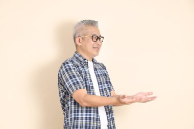 Gözlüklü, kareli gömleği, şortu ve spor ayakkabısı giyen, bej arka planda izole edilmiş Asyalı son sınıf öğrencisinin portresi. Yaşlı erkek yaşam tarzı konsepti.