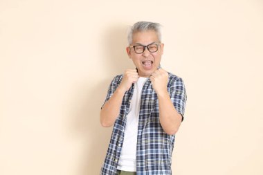 Gözlüklü, kavgacı, sıradan ekose gömlekli, şortlu ve bej arka planda izole edilmiş spor ayakkabılı Asyalı bir adamın portresi. Yaşlı erkek yaşam tarzı konsepti.