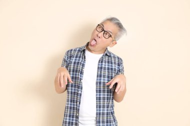 Gözlüklü, aptal, sıradan ekose gömlek, şort ve spor ayakkabı giyen, bej arka planda izole Asyalı son sınıf öğrencisinin portresi. Yaşlı erkek yaşam tarzı konsepti.