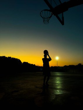 Plajda elinde basketbol topu olan bir adamın silueti.