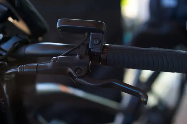 Close-up view of a bicycle brake lever with a rubberized grip, along with an E-bike control on the handlebar. No person, only the handlebar with the brake lever.