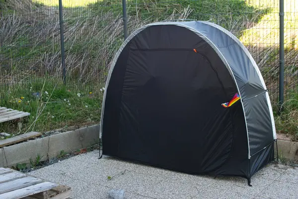 Stock image Closed black tent with a rainbow flag inserted into the closure. Context: camping, LGBTQ+, gay, lesbian, homosexual, bisexual, sexuality, enclosure, solitude, togetherness, hiding, separation, privacy, gender, unity.