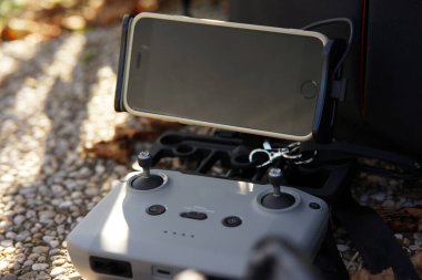 Uzaktan kumandalı uzaktan kumandalı uzaktan kumandalı bir uzaktan kumanda ve cep telefonu tutacağı. Kapıya siyah ekranlı bir akıllı telefon yerleştiriliyor. Uzaktan kumanda, görünür joysticklerle beton bir yüzeyde. Arka planda hafif bir bulanıklık var.
