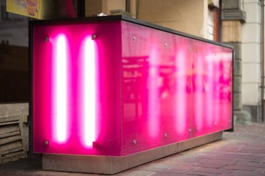 Neon tüplerle aydınlatılmış pembe arka aydınlatma cepheleriyle bir açık hava bar tezgahının hareketli atmosferini keşfedin. Yayaların açık havasında yer alan bu boş bar, çağdaş ve davetkar bir atmosfer yayıyor. İnsanların yokluğu onların...