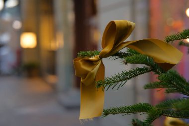 Bir Tannenbaum dalında süslenmiş altın kumaştan bir kurdeleyle tatil ve Noel alışverişini görselleştirin. Arkaplanda kırmızı, pembe, mavi ve sarı renkli canlı renkler var. Büyüleyici bir bokeh etkisi yaratıyor.
