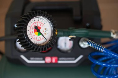 Arka planda yeşil kompresör ve mavi spiral hortumla analog hava basıncı göstergesi.