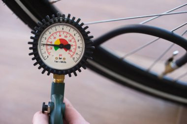 Elinde bir lastik basıncı göstergesi var. 2,2 bar ya da 31 psi. Arka planda bulanık bisiklet lastiği var. İçerik: şişirilmiş bisiklet lastikleri, hava, izleme, bisiklet güvenliği, servis.
