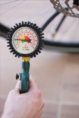Elinizde bir lastik basıncı göstergesi var. 2,3 bar ya da 32 psi. Arka planda bulanık bisiklet lastiği var. İçerik: şişirilmiş bisiklet lastikleri, hava, izleme, bisiklet güvenliği, servis.