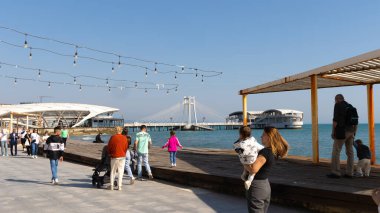 Durres, Arnavutluk - 13 Nisan 2024 - Durres gezinti sahasında ahşap bir platform boyunca yürüyen insanlarla fotoğraf