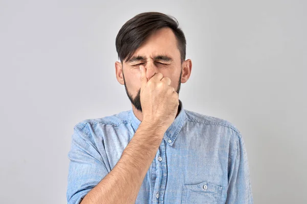 鼻を持っている若い男は うんざりした匂い 指で鼻と口をつまむと白い背景に隔離された息を保持する — ストック写真