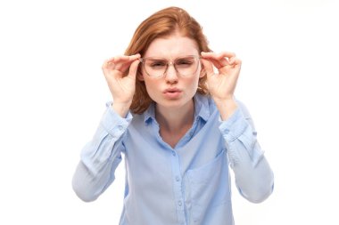 Kızıl saçlı, gözlüklü genç bir kadın beyaz arka planda izole edilmiş kameraya bakarken gözlerini kısıyor. Görüş sorunları kavramı