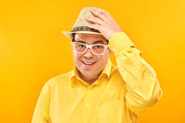Sarı arka planda izole edilmiş, şapkalı, gülümseyen şişman bir adamın portresi. Seyahat konsepti.