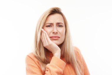 Yüzünde acı çeken bir ifade olan genç sarışın kadın, ellerinin yanaklarını tutuyor, beyaz arka planda avuç içi izole edilmiş ağızlara dokunuyor. Diş ağrısı, diş ağrısı konsepti