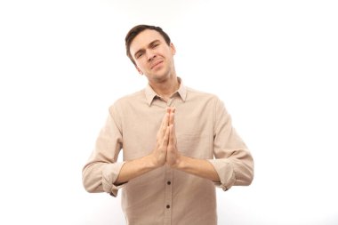 Genç esmer adamın portresi beyaz arka planda izole edilmiş dua hareketleriyle ellerini kavuşturdu. Huzurlu, müteşekkir, güvenilir, bir dilek konsepti