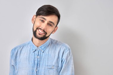 Beyaz stüdyo arka planında izole edilmiş beyaz tenli, esmer, sakallı, olumlu gülümseyen erkek portresi.