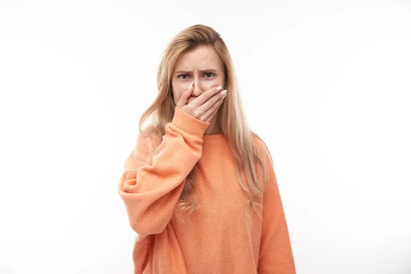 Young blonde woman holding nose to avoid disgusted smell, pinches nose and mouth with fingers and holding breath isolated on white background