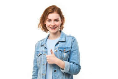 Genç kızıl saçlı kadın elini kaldırıyor ve beyaz arka planda izole kameraya gülümsüyor.