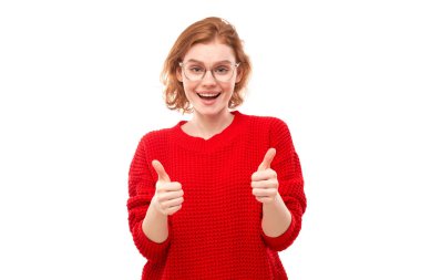 Genç kızıl saçlı kadın elini kaldırıyor ve beyaz arka planda izole kameraya gülümsüyor.