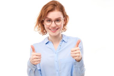 Genç kızıl saçlı kadın elini kaldırıyor ve beyaz arka planda izole kameraya gülümsüyor.