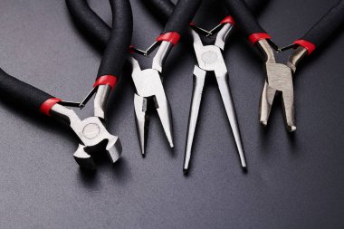 Farklı tipte pense ve yan kesiciler siyah arkaplanda izole edilmiş. Tamir, inşaat ve bakım için el aletleri