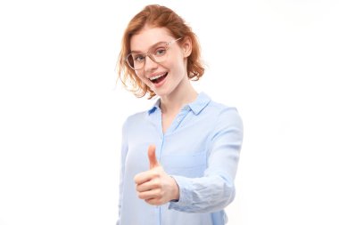 Genç kızıl saçlı kadın elini kaldırıyor ve beyaz arka planda izole kameraya gülümsüyor.