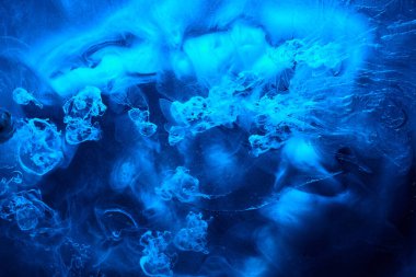 Blue abstract ocean background. Splashes and waves of paint under water, clouds of smoke in motion.