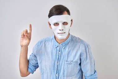 Yüzünde beyaz maskeli gizemli adam stüdyo arka planında izole edilmiş.