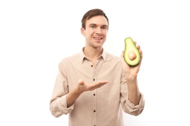 Beyaz stüdyo arka planında izole edilmiş yarım bir avokado gösteren ve gülümseyen yakışıklı beyaz esmer adamın portresi.