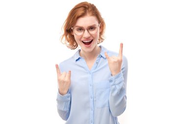 Genç kızıl saçlı kadının portresi beyaz arka planda izole edilmiş parmaklarıyla rock 'n roll hareketi gösteriyor.